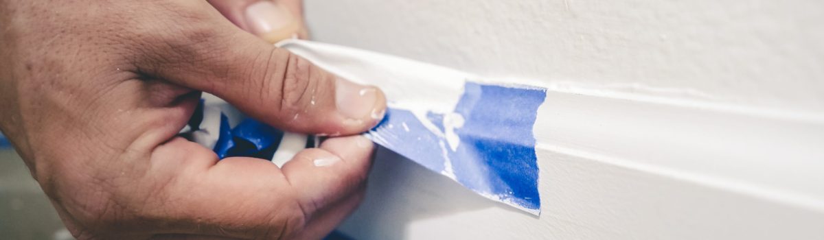 Painter Man Removing Masking Blue Tape From Molding, Baseboard.